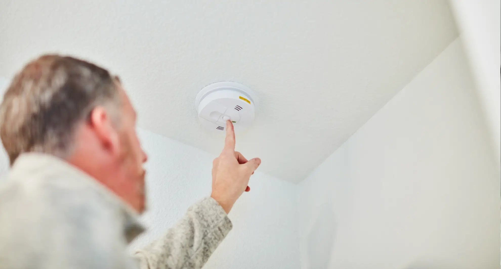 Person testing carbon monoxide detector on ceiling