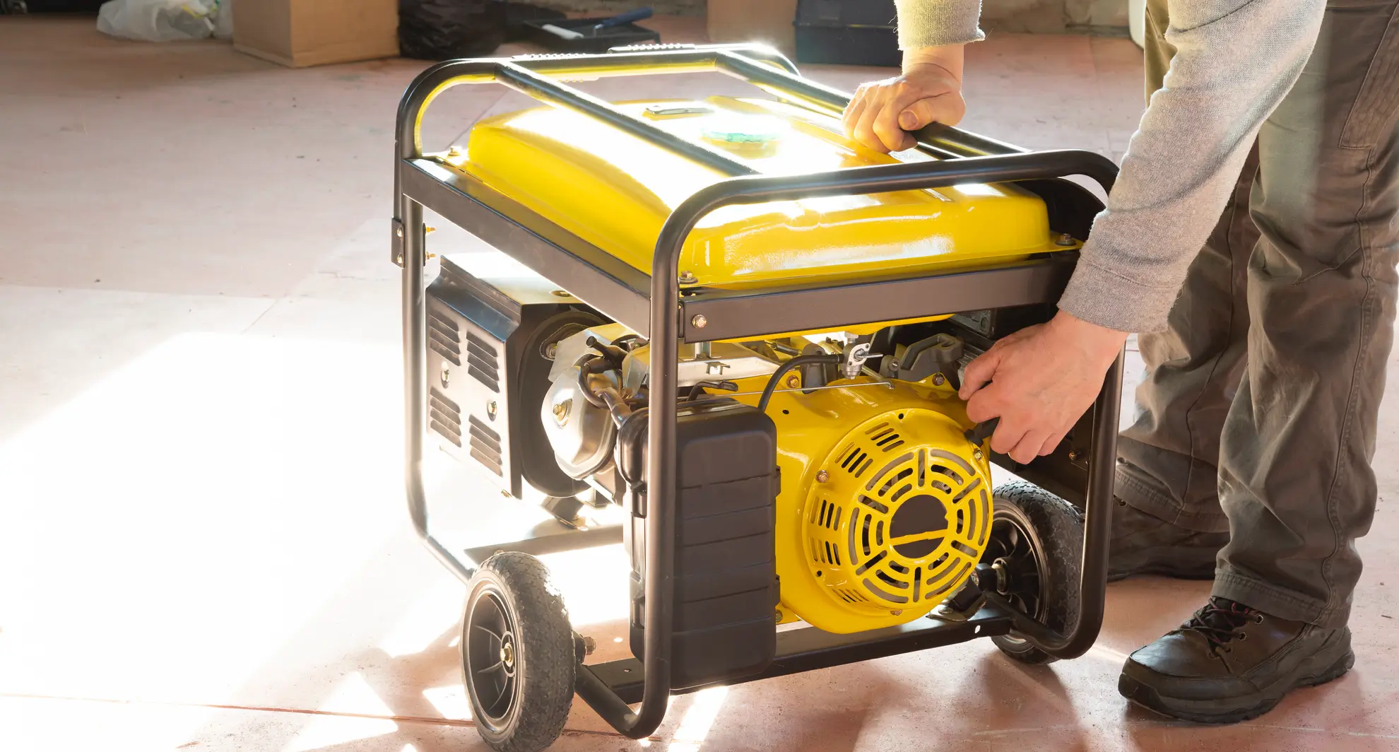 Worker servicing portable yellow commercial generator, pulling start cord inside facility