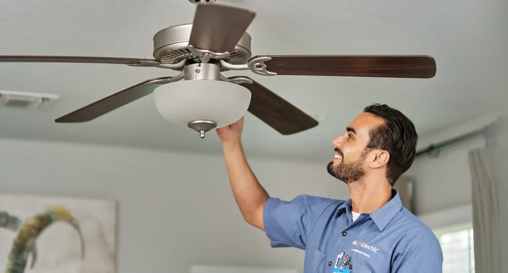 A skilled electrician in a blue uniform is installing a ceiling fan