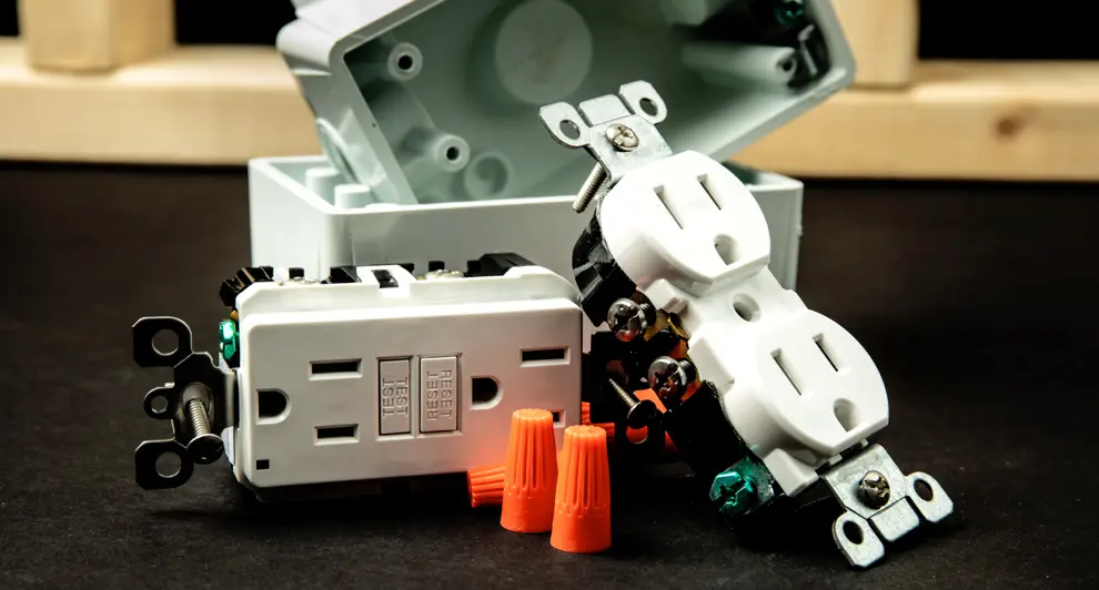 Electrical outlets, wiring connectors, and a junction box displayed on a black surface