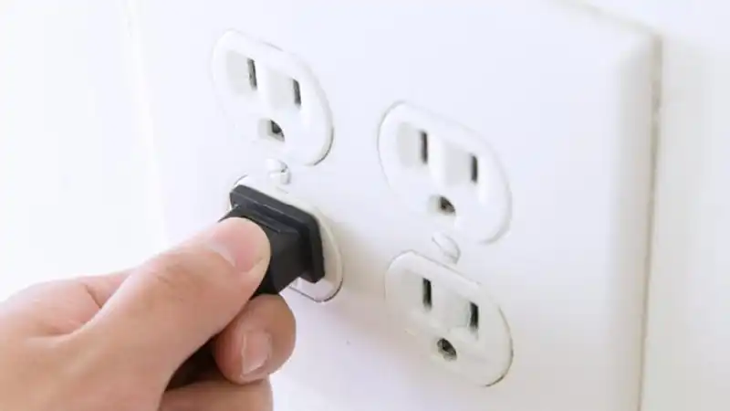 Hand plugging cord into three-pronged wall outlet.